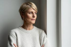 Blonde middle-aged woman in a gray sweater looking out a window