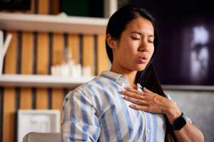 Woman in a blue an white striped shirt with a hand on her chest practicing slowed breathing