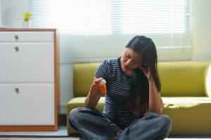Woman sitting on the floor in front of a yellow couch holding an orange pill bottle