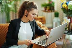 Businesswoman on an orange couch balancing a laptop on the arm of the couch