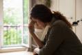 Woman in shadowed lighting sitting and touching her forehead