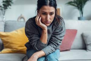 Woman in a gray sweater zoning out, sitting on a gray couch