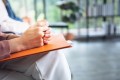 Woman sitting with hands clasped on a notebook, waiting nervously before a presentation or meeting
