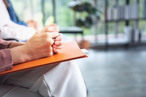 Woman sitting with hands clasped on a notebook, waiting nervously before a presentation or meeting
