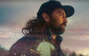 Picture Noah Kahan in a baseball cap looking at a sunset superimposed over an image of him in a white shirt performing at Fenway Park