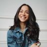 Dark-haired woman sitting and smiling wearing a denim jacket