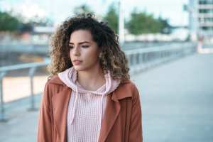 Woman in a pink knit sweatshirt and orange jacket walking by a canal