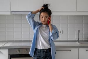 Distressed woman in a kitchen talking on a red cell phone