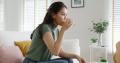 Woman in a green sweater on a white couch is taking medication with water