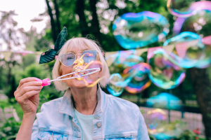 Older woman in denim jacket and a green headband blowing bubbles