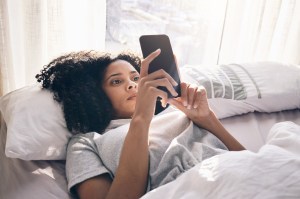 Women laying in bed staring at her phone, using an AI chatbot for mental health