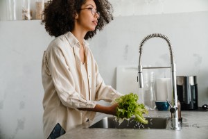 Woman standing at home sink washing lettuce, looking concerned