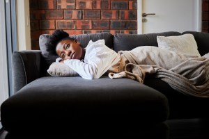 Young woman laying on couch looking bored in her living room, possibly feeling anhedonia