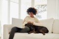 Woman home alone, sitting on couch with her dog, laptop on her lap