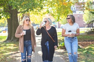Three women friends walking and talking in a park with coffee